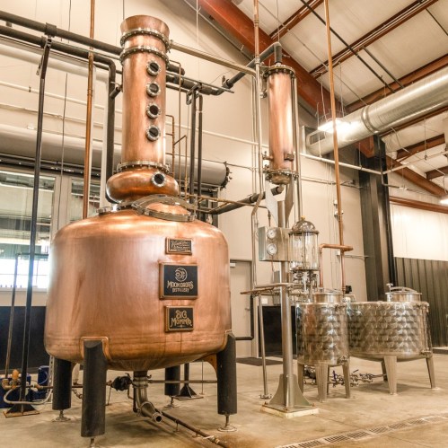 A large copper distillation apparatus in a modern industrial setting, with stainless steel tanks and pipes.