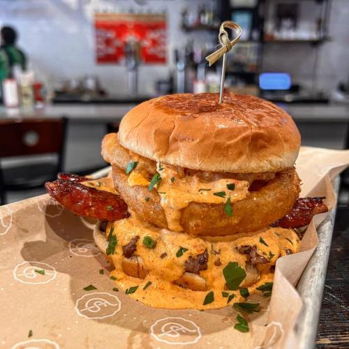 A close-up of a shrimp burger with a toasted bun, topped with creamy sauce and garnished with parsley, served on a plate.