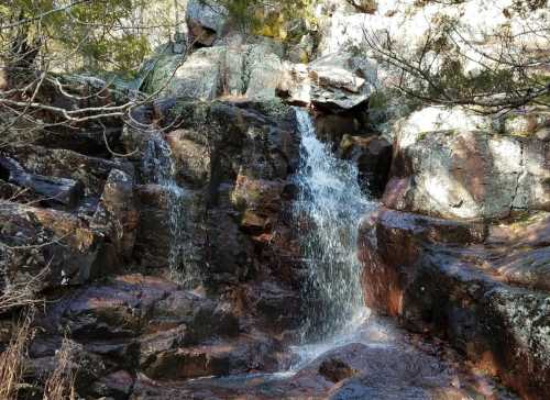 A small waterfall cascading over rocky terrain, surrounded by trees and natural vegetation.