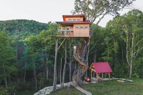 A treehouse perched high in a tree, featuring a spiral staircase and surrounded by lush greenery and mountains.