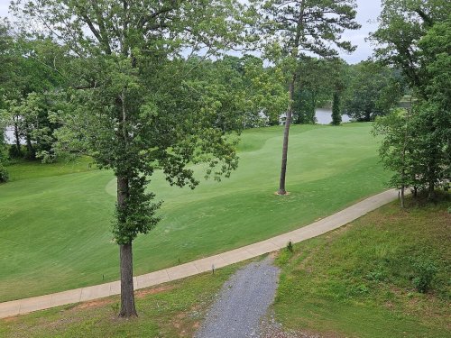 A serene view of a golf course with lush green grass, trees, and a pathway leading to a nearby lake.
