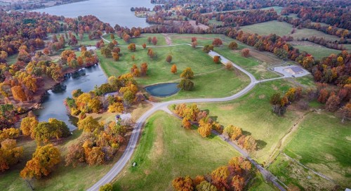 Aerial view of a scenic landscape with colorful autumn trees, a pond, and winding roads near a lake.