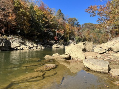 A serene river scene surrounded by autumn foliage and rocky banks under a clear blue sky.