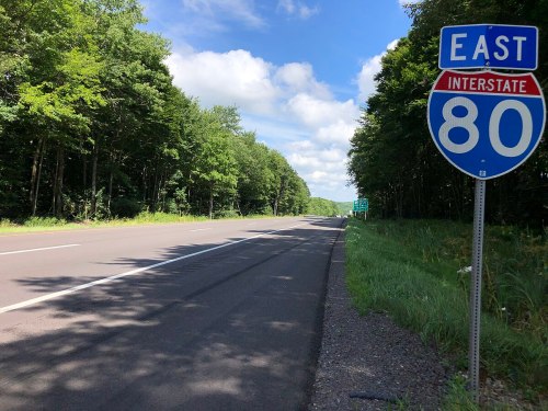 A view of a highway with a blue interstate sign indicating I-80 East, surrounded by trees and a clear sky.