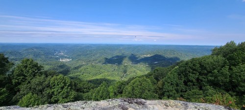 A panoramic view of lush green mountains under a clear blue sky, with distant hills and valleys visible.