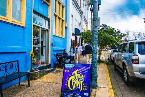 A colorful blue building with people gathered outside, featuring a sign for an art and food music event.