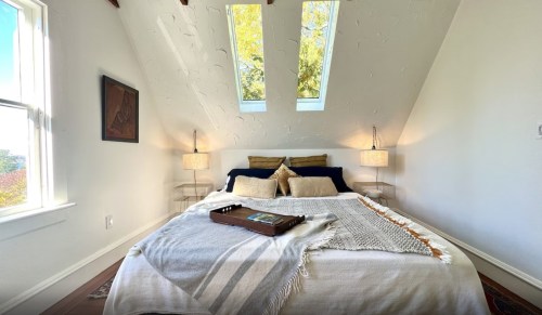 Cozy bedroom with a bed, two lamps, and skylights, featuring a warm color palette and decorative throw.