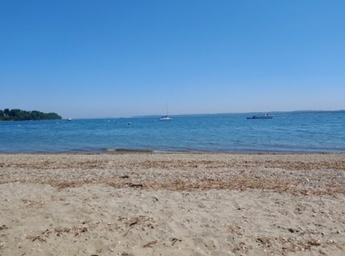 A serene beach scene with clear blue water, a sandy shore, and a few boats in the distance under a bright blue sky.