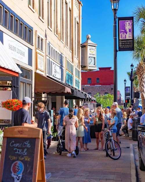A bustling downtown street with people walking, shopping, and enjoying the atmosphere on a sunny day.