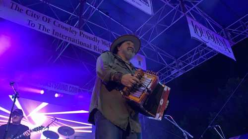 A musician plays an accordion on stage, illuminated by colorful lights during a live performance.