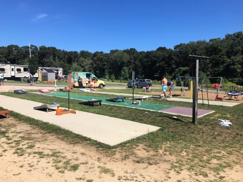 A sunny park scene with playground equipment, picnic tables, and people enjoying outdoor activities.