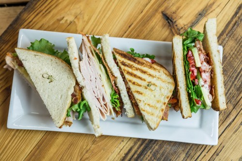 A platter of sliced sandwiches with turkey, lettuce, tomato, and mayonnaise on toasted bread, arranged neatly.