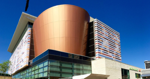 Modern building with a large copper dome and colorful striped facade against a clear blue sky.