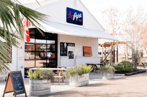 Exterior of a BBQ restaurant named "Pure BBQ," featuring a welcoming sign and outdoor seating with plants.