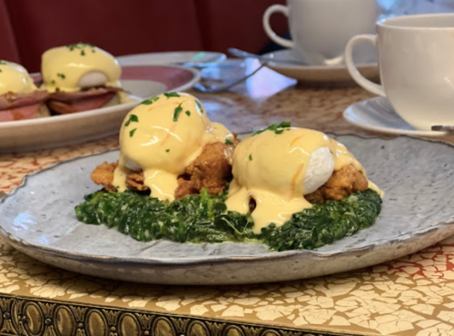 A plate of eggs Benedict with poached eggs, hollandaise sauce, and fried chicken on a bed of sautéed greens.