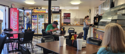 A casual diner interior with customers at tables, a counter, and a display of food and drinks in the background.