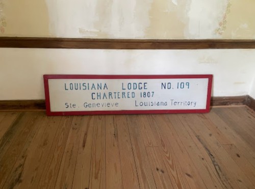 Sign for Louisiana Lodge No. 109, chartered in 1807, displayed on a wooden floor in a room with peeling walls.