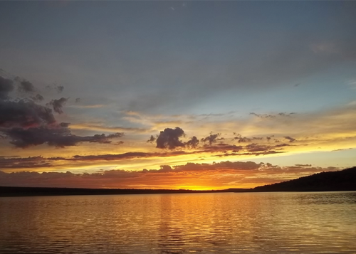 A serene sunset over a calm lake, with vibrant orange and purple hues reflecting on the water's surface.