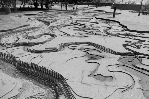 A black and white image of a textured, wavy concrete surface resembling a topographic map in an outdoor setting.