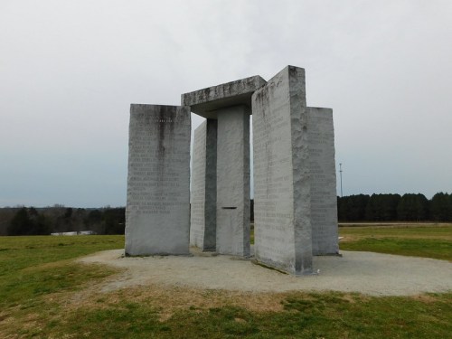 A stone monument with large slabs inscribed with text, set in a grassy area under a cloudy sky.
