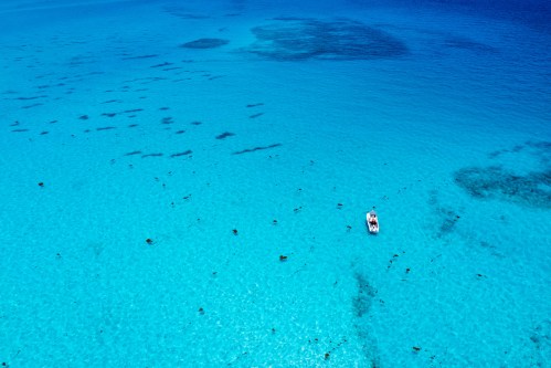Aerial view of a clear blue ocean with people swimming and a small boat in the water.