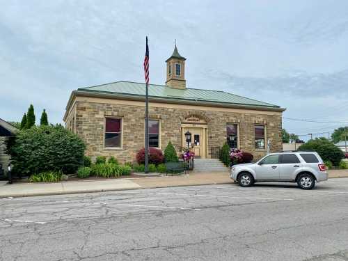 Historic stone building with a clock tower, American flag, and landscaped front, viewed from the street.