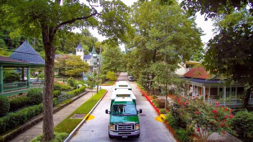 A tree-lined street with green trucks parked, surrounded by charming houses and lush greenery.