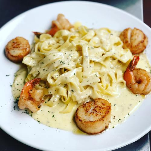 Creamy fettuccine pasta topped with shrimp and seared scallops, garnished with herbs on a white plate.