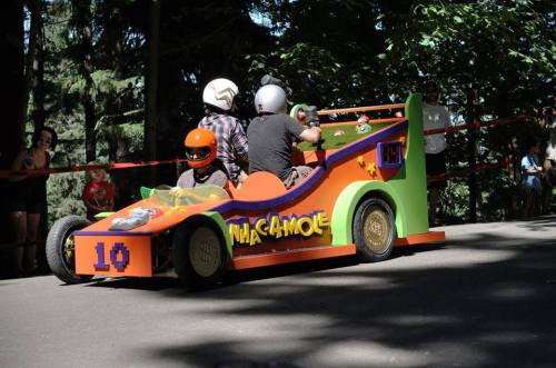 A colorful go-kart with a cartoon theme, racing down a tree-lined path, with three riders wearing helmets.