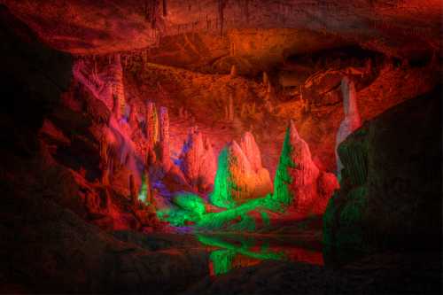 Colorful illuminated cave with stalagmites and stalactites reflecting in water, creating a mystical atmosphere.