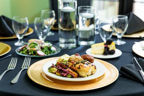 A beautifully arranged table with a plate of roasted vegetables, chicken, rice, salad, and dessert, set with elegant glassware.