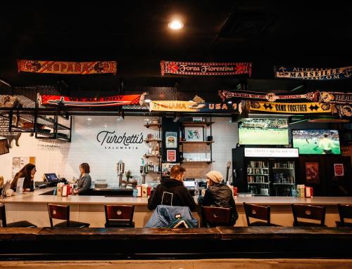 A cozy bar with patrons sitting at the counter, decorated with sports memorabilia and a TV showing a game.