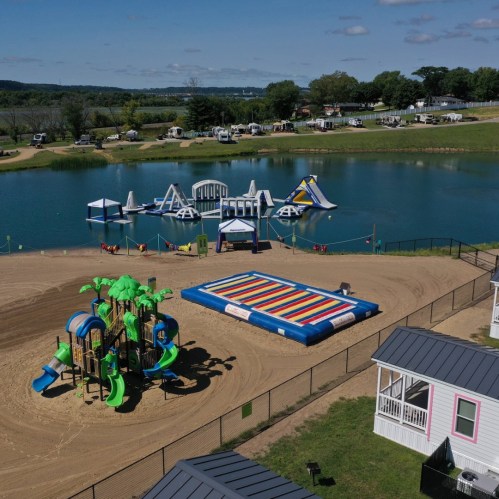Aerial view of a sandy beach area with inflatable water attractions and a colorful playground near a lake.