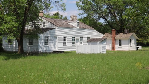 Two white historic houses surrounded by green grass and trees under a clear blue sky.