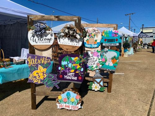 A display of colorful wooden signs at a market, featuring welcoming messages and floral designs.