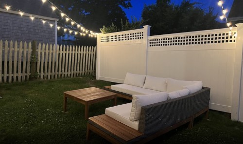 Cozy outdoor seating area with a sofa and table, illuminated by string lights against a darkening sky.