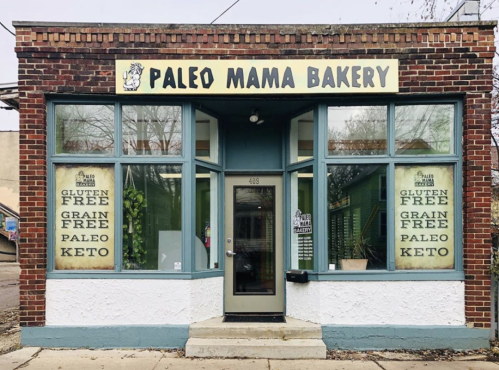 Exterior of Paleo Mama Bakery, featuring large windows and signs for gluten-free, grain-free, paleo, and keto options.