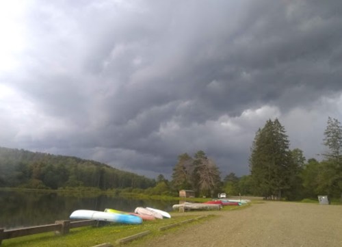 A serene lakeside scene with colorful kayaks on the shore under a dramatic, cloudy sky.