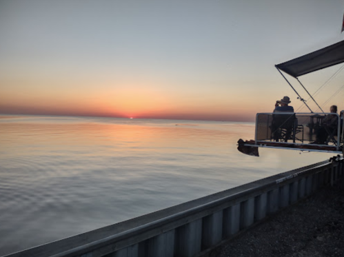 A serene sunset over calm waters, with silhouettes of people enjoying the view from a dock.