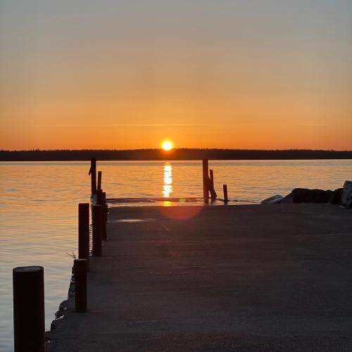A serene sunset over calm waters, viewed from a wooden dock extending into the lake.