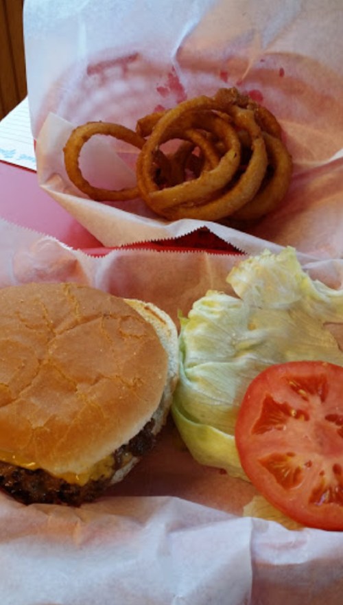 A burger with lettuce and tomato, served with a side of curly fries on a red table.