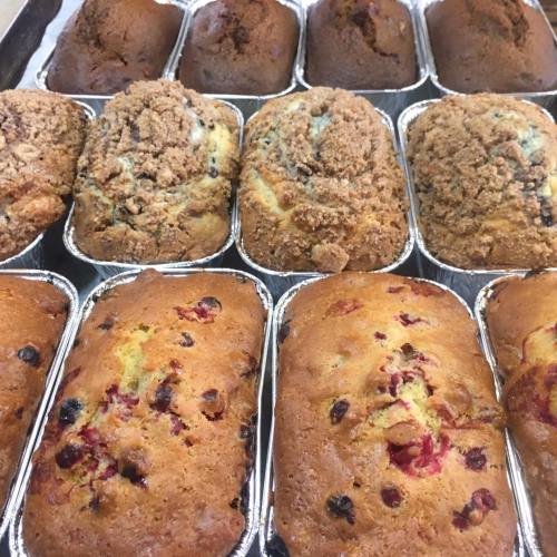 A variety of freshly baked loaves, including fruit and crumb-topped varieties, arranged in metal trays.