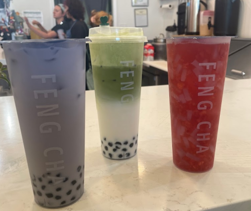 Three colorful drinks with boba on a counter, labeled "FENG CHA," in a cafe setting.