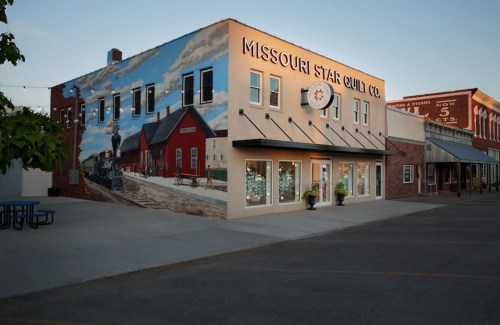 Exterior of Missouri Star Quilt Co. building with a mural, featuring a train and a quaint town setting.