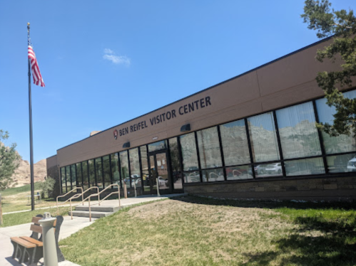 Exterior of the Ben Reifel Visitor Center with large windows, a flagpole, and a grassy area in front.