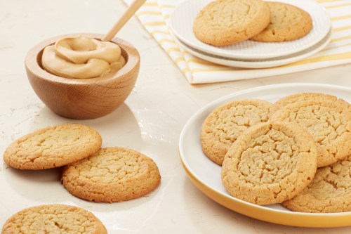 A plate of golden cookies next to a bowl of creamy peanut butter on a light countertop.