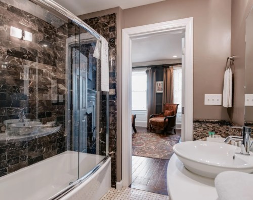 Modern bathroom featuring a curved glass shower, marble walls, and a view into a cozy living area.