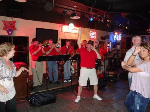 A lively band performs on stage while people dance and enjoy the music in a vibrant bar setting.