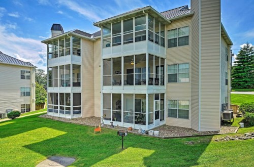 A multi-story apartment building with screened porches, surrounded by green grass and trees under a blue sky.
