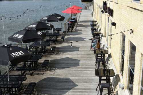 Outdoor dining area with black and red umbrellas along a wooden boardwalk by the water.